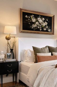 a bed with white sheets and pillows in a bedroom next to a painting on the wall