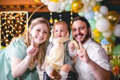 a man and woman holding a baby in front of balloons