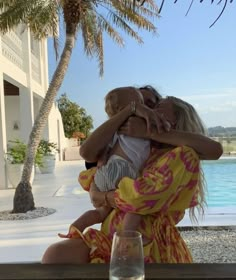 a woman holding a baby while sitting next to a pool