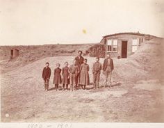 an old black and white photo of people standing in front of a small house on a hill