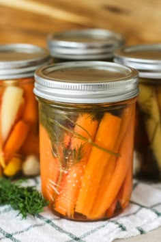 three jars filled with pickles and carrots on top of a cloth covered table