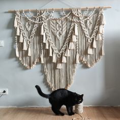 a black cat standing next to a macrame wall hanging