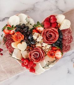 a heart shaped platter filled with fruit and cheese on top of a marble table