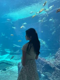 a woman standing in front of an aquarium looking at the fish swimming by her side