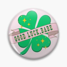 a button with the words good luck babe written on it and shamrocks in gold stars