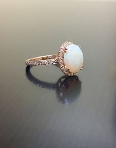 DeKara Designs Collection Our latest design! An elegant and lustrous Opal cabochon surrounded by beautiful diamonds in a halo setting. Metal- 18K Rose Gold, .750. This Specific Ring Is a Size 6 3/4 Stones- Center Features an Oval Fiery Australian Opal Cabochon Cut 2.20 Carats, 11.10 MM Long, 9 MM Wide, 44 Round Diamonds, H-I Color VS2-SI1 Clarity, 0.40 Carats. Latest of my creations. A beautiful Opal Halo Diamond Ring. The Opal is professionally prong set in between 4 double prongs. There are 10 Exquisite Rose Gold Rings With Halo Design, Luxury Rose Gold Opal Gemstone Ring, Formal Rose Gold Opal Ring With Diamond, Luxury Rose Gold Opal Ring, Elegant Oval Opal Ring, Elegant White Gold Opal Ring, Luxury White Rings For Proposal, Luxury White Oval Cabochon Ring, Elegant Opal Ring With Prong Setting