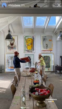 two people standing in front of a table with food on it and paintings hanging above