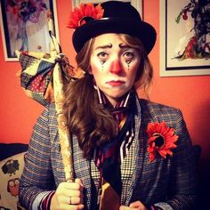 a woman dressed as a clown holding a stick with flowers on her nose and wearing a top hat