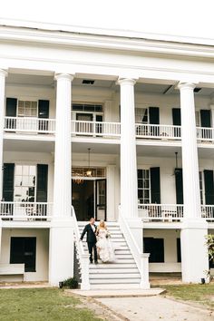 a bride and groom walking up the steps of a large white building with black shutters