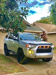 a silver toyota truck parked in front of a house next to a tree with green leaves