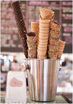 ice cream cones in a bucket with sprinkles and chocolate on the side