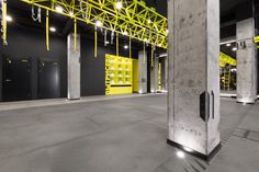 an empty room with yellow and black lighting on the ceiling, and concrete columns in the center