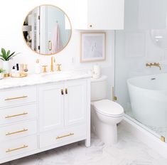 a white bathroom with gold accents and marble counter tops, along with an oval mirror on the wall