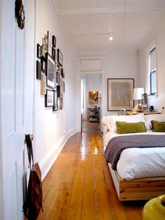 a bedroom with wood flooring and white walls has pictures on the wall above the bed