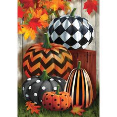 three pumpkins are sitting on the grass near some flowers and other autumn decorations in front of a wooden fence