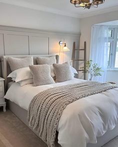 a bed with white linens and pillows in a bedroom next to a large window