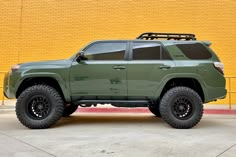 a green toyota truck parked in front of a yellow wall with black wheels and tires