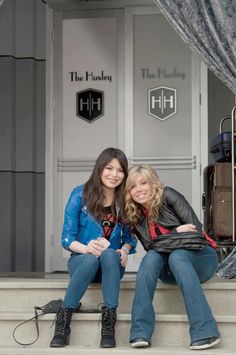 two women sitting on the steps in front of a building with their arms around each other