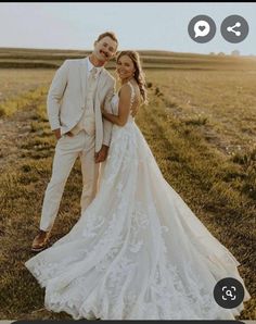 a bride and groom standing in the middle of an open field, posing for a photo