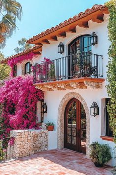 a white house with pink flowers on the balcony and balconies over it's doors