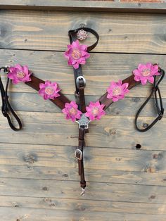 a horse bridle decorated with pink flowers on a wooden background and brown leather reins