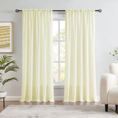 a living room with a white couch and large window covered in light yellow drapes