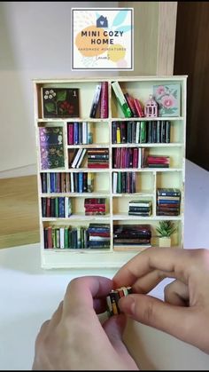 two hands are holding small objects in front of a bookshelf filled with books