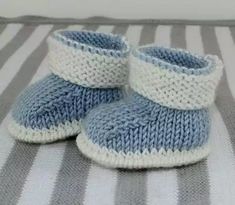 a pair of blue and white knitted baby booties sitting on a striped blanket