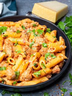 pasta with meat and parsley in a skillet next to cheese on the side