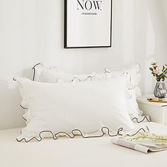 a white bed topped with pillows next to a framed poster on the wall above it