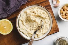 hummus in a bowl with garlic, lemon and peanuts on the side next to it