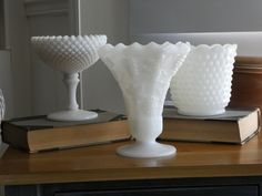 three white glass vases sitting on top of a wooden table next to an open book