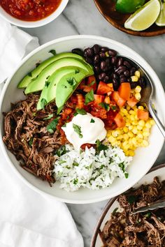 a bowl filled with shredded beef, beans, avocado, corn and tomatoes