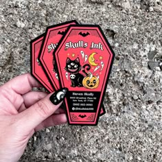 a hand holding two red and black stickers on top of a cement ground next to rocks