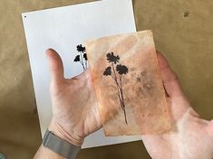 a person holding up an old piece of paper with flowers on it in their hand