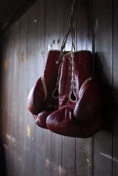 two red boxing gloves hanging from a hook on a wooden wall in a dark room