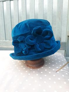 This is a turquoise teal blue cloche hat made from brightly coloured soft velvet and lined with polycotton. Decorated with two 3d flowers to give it an individual look. Wear it low over the ears to keep the wind at bay. It's robust enough to keep you dry during Autumn showers and warmer on those cooler spring days. This hat has more than just a hint of the Autumnal/wintery 1920's style about it with it's classic cloche hat shape.  Our hats are made to a size specified by you. Simply measure arou Flower Cloche, Red Bucket Hat, 1920s Hat, Blue Bucket Hat, Vintage Style Hat, Holiday Hats, Warm Winter Hats, Blue Winter, Chemo Hat