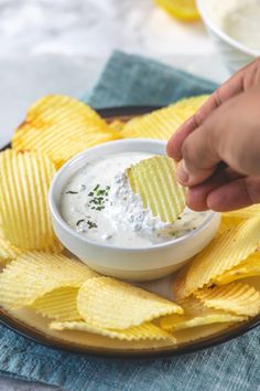 a person dipping chips into a bowl of white sauce on a plate with other food