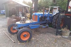 an old blue tractor parked in front of a shed with orange rims and tires