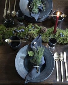 a place setting with silverware and greenery on the table, including an evergreen centerpiece