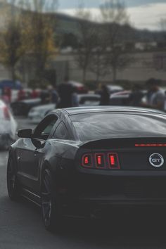 a black car driving down a street with lots of cars in the backround