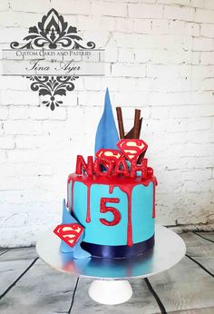 a birthday cake decorated with the number five and supermans on top is sitting on a table in front of a brick wall