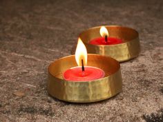 two gold candles sitting on top of a stone floor next to each other with one burning