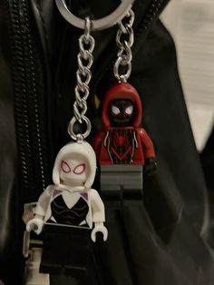 two lego figurines sitting on top of a black bag with a spiderman keychain attached to it