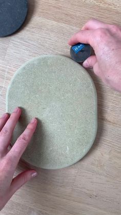 two hands are using a mouse to push the button on a round object that is sitting on a wooden table