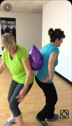 two women are doing exercises with balloons in an office building, one is holding a purple ball and the other has a green shirt