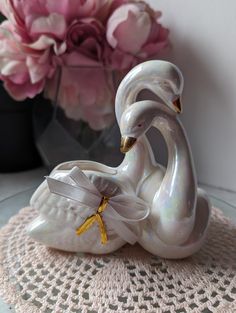 a white swan figurine sitting on top of a table next to pink flowers