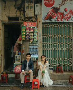 a man and woman sitting on red chairs in front of a storefront with coca - cola signs