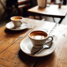 two cups of coffee sitting on top of a wooden table next to eachother