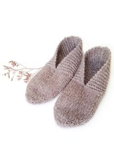 a pair of gray knitted slippers sitting on top of a white floor next to a plant